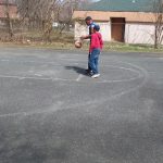 Two people playing basketball outdoors on an asphalt court near a building.