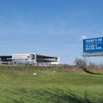 Billboard advertising "Auto Lenders" next to a grassy field and road under a blue sky.