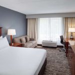 Modern hotel room with large bed, sofa, desk area, and window view.