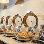 Buffet line with chafing dishes and large, decorative metal rings on a white tiled counter.