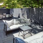 Modern outdoor patio with grey decking, contemporary lounge furniture, and tall privacy fencing.