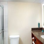 Modern bathroom with glass shower, beige textured wall, and granite vanity.