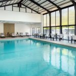 Indoor swimming pool area with large windows overlooking an outdoor patio and seating.