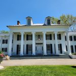 Neoclassical white house with columns and blue sky backdrop.