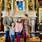 Family posing in a grand hall with an ornate fireplace and bookshelves.