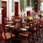 Elegant dining room with a fireplace, patterned wallpaper, and set tables for a formal meal.