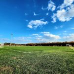 Soccer field under a bright blue sky with scattered white clouds.