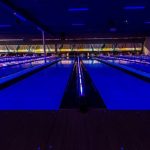 Indoor swimming pool illuminated with vibrant blue and purple lights at night.