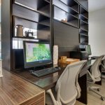 Modern office space with dark shelving, computer monitor displaying a soccer field, and ergonomic chairs.