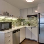 Modern kitchen with white cabinets, stainless steel appliances, and green subway tile backsplash.