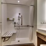 Modern white shower with fixtures and a bench next to a bathroom vanity.
