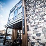 Modern building facade with glass windows and stacked stone exterior next to outdoor seating area.