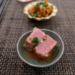 Seared tuna slices in a small bowl on a woven mat, with a side dish of relish.