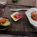Assortment of small dishes on a woven mat, including red meat and seafood.