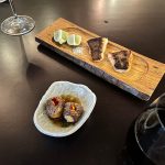 Charred bread and small meat bites served on a dark table with wine glass.