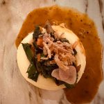 Savory dish with poached egg, greens, and toppings in a rich brown sauce.
