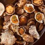 Assortment of roasted and raw oysters, clams, and seafood in a dark metal serving dish.