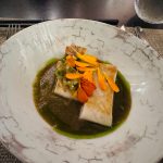 Gourmet dish of white fish in green sauce, garnished with edible orange flowers.