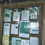 Informational board detailing park rules, trails, and wildlife in a wooded area.