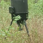Camouflaged military observation post mounted on tripod in dense woods.