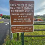Park sign detailing rules: hours, no alcohol/vehicles, leash law, and permit access.