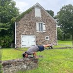 Man doing a handstand on a stone wall in front of an old stone house.