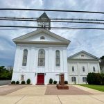 White church with steeple and adjacent white building under a cloudy sky.