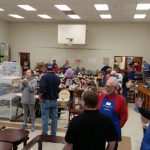Indoor craft fair or market with tables displaying various handmade goods and people browsing.