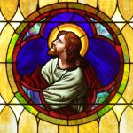 Stained glass window depicting Jesus Christ in a circular medallion, surrounded by warm gold light.