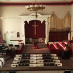 Interior view of a church sanctuary with altar, organ pipes, and pews.