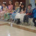 Young girls in costumes perform on a stage indoors.