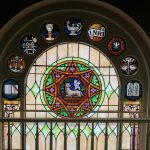 Stained glass window featuring a central circular design with an animal motif and religious symbols above.