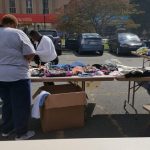Donations laid out on tables outdoors near commercial buildings under a partly cloudy sky.