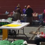 People gather outside a red building at an outdoor market or event.