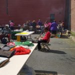 People gather outside a large red building at an outdoor market or event.