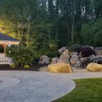 Gazebo with warm light and landscaped rock garden at twilight.