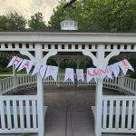 White gazebo with "HAPPY SUMMER" banner under green trees.