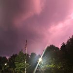 Dramatic pink and purple sunset sky over a park with trees and an American flag.