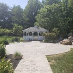 White gazebo in a lush, green park setting with stone pathways.