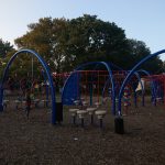 Colorful playground equipment with blue arches set against a backdrop of trees under a clear sky.