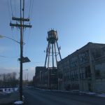 Industrial scene with a tall metal tower and large factory building under a blue sky.