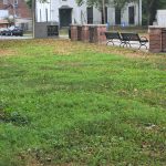 Green lawn in front of a white historic building with black benches.