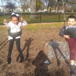 Two children swing in a park, one girl and one boy, on a sunny day.