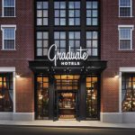 Graduate Hotels facade with large windows and illuminated entrance at night.