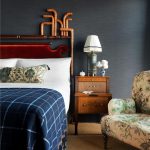Dark bedroom with a rich red headboard, blue plaid duvet, and an ornate side table.
