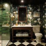 Luxurious bathroom with green tile shower and dark forest-themed wallpaper.