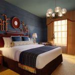 Luxury hotel bedroom with dark blue textured walls, large bed, and ornate chandelier.