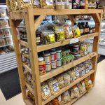 Wooden shelving unit stocked with various dried herbs, spices, and bulk goods in a store setting.