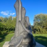 Abstract granite sculpture set outdoors against a bright blue sky and green trees.