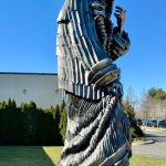 Bronze sculpture of a powerful, stylized figure standing outdoors against a blue sky.